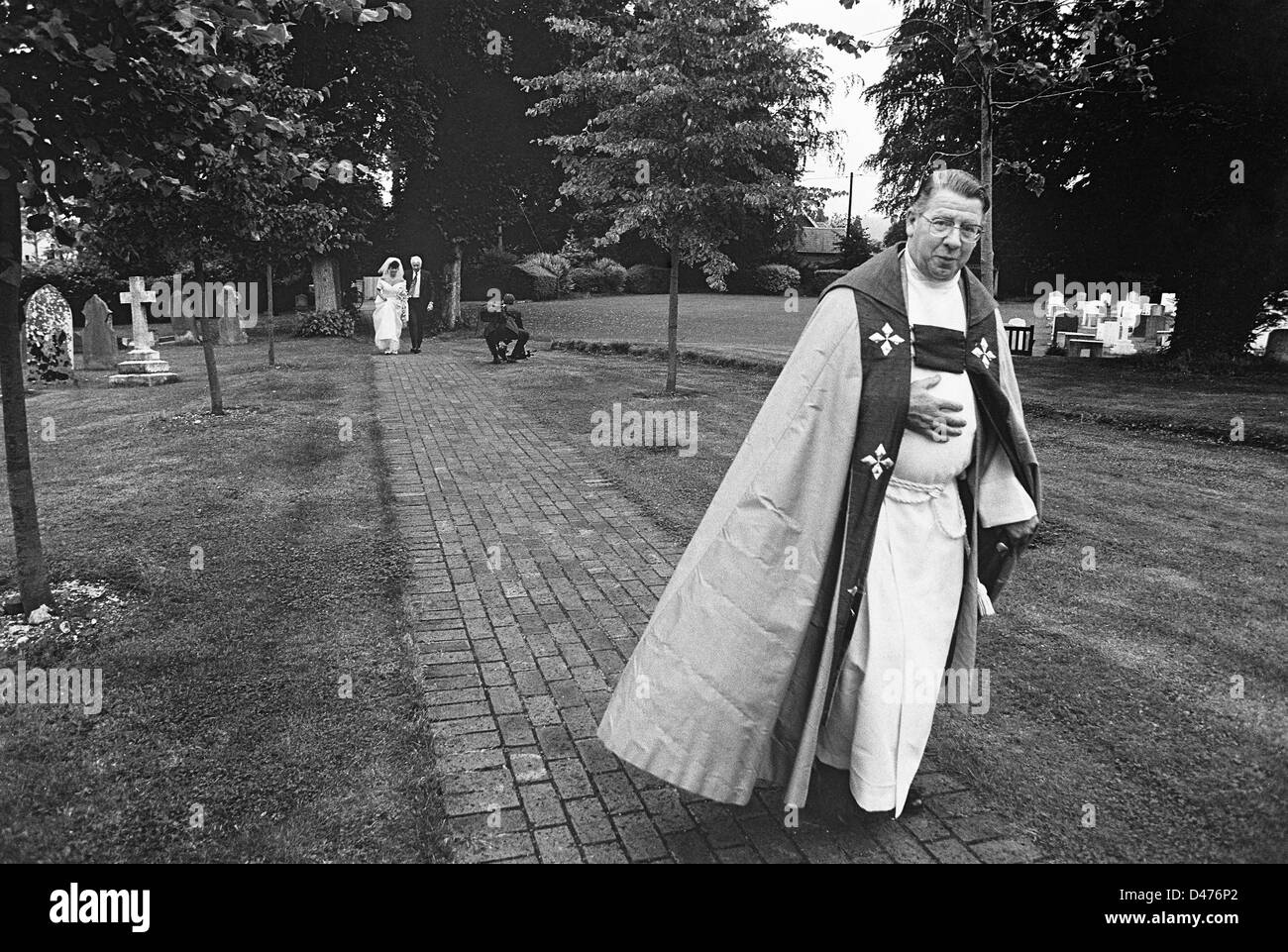 Eine Braut mit ihrem Vater folgt der Pfarrer durch den Kirchhof, verheiratet zu sein Stockfoto