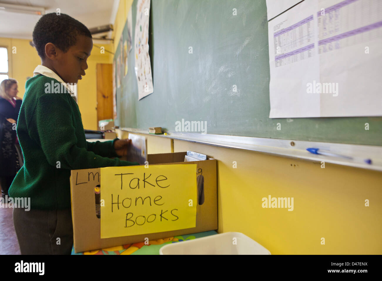 Kleiner Junge entscheidet welche Bücher mit nach Hause nehmen. Schülerinnen und Schüler im Lesen / Alphabetisierung Klasse, Cape Town, Südafrika. Stockfoto