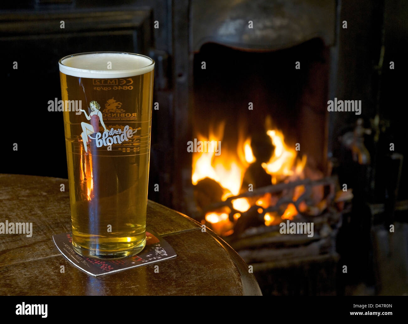 Ein Pint Bier Dizzy Blondine auf einem Pub-Tisch mit offenem Feuer im Hintergrund Stockfoto