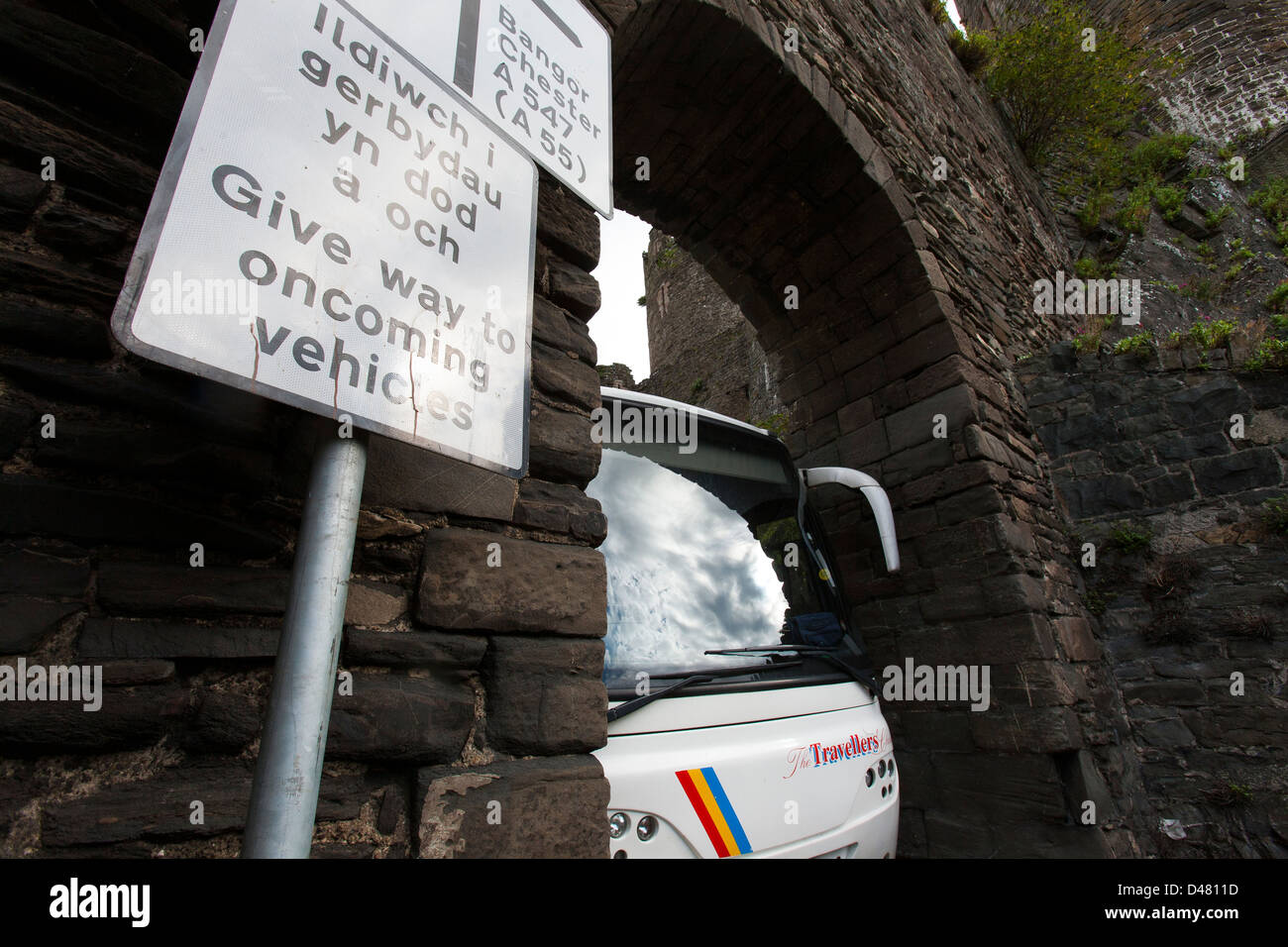 Ein großen Passagier-Coach bus quetscht durch einen alten steinernen Torbogen oder Brücke in Nord-Wales Stockfoto