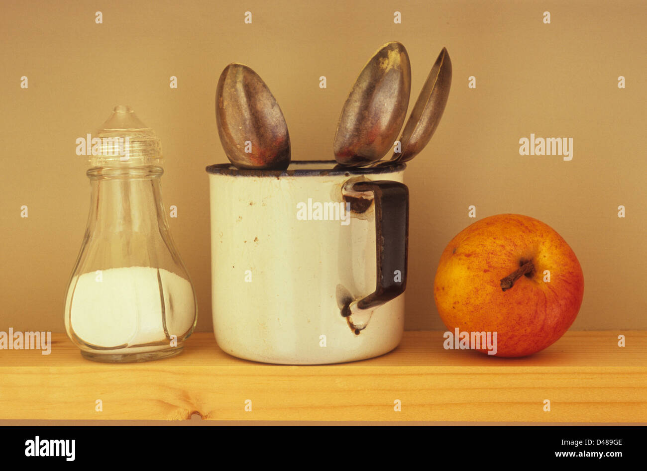 Augenhöhe Blick auf schmalen Holzregal mit halbvollen durchsichtigen Kunststoff Salz Menage Emaille Becher mit drei Teelöffel und Apfel Stockfoto
