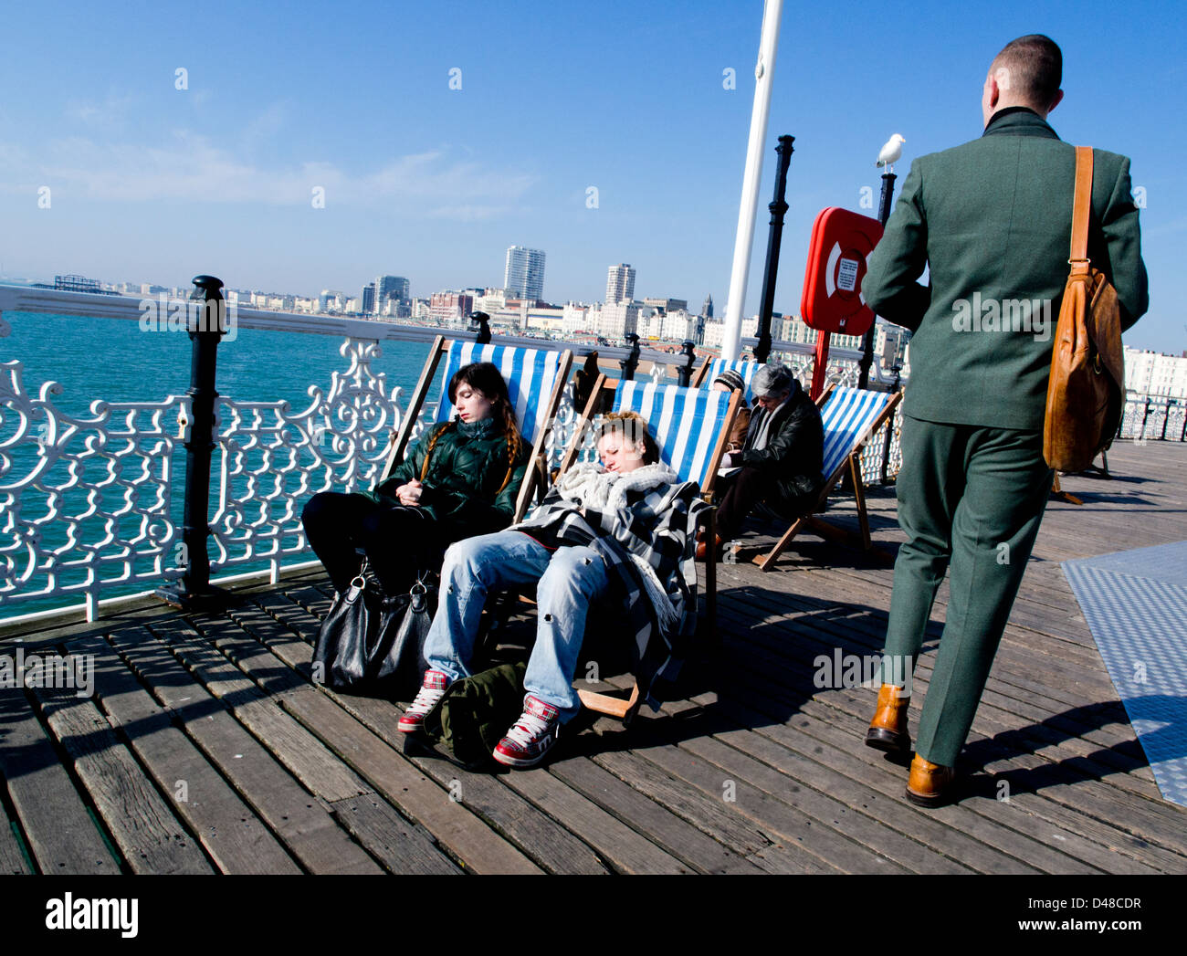 Zwei Studenten Mädchen dösen auf Liegestühlen in der Frühlingssonne am Pier von Brighton Stockfoto