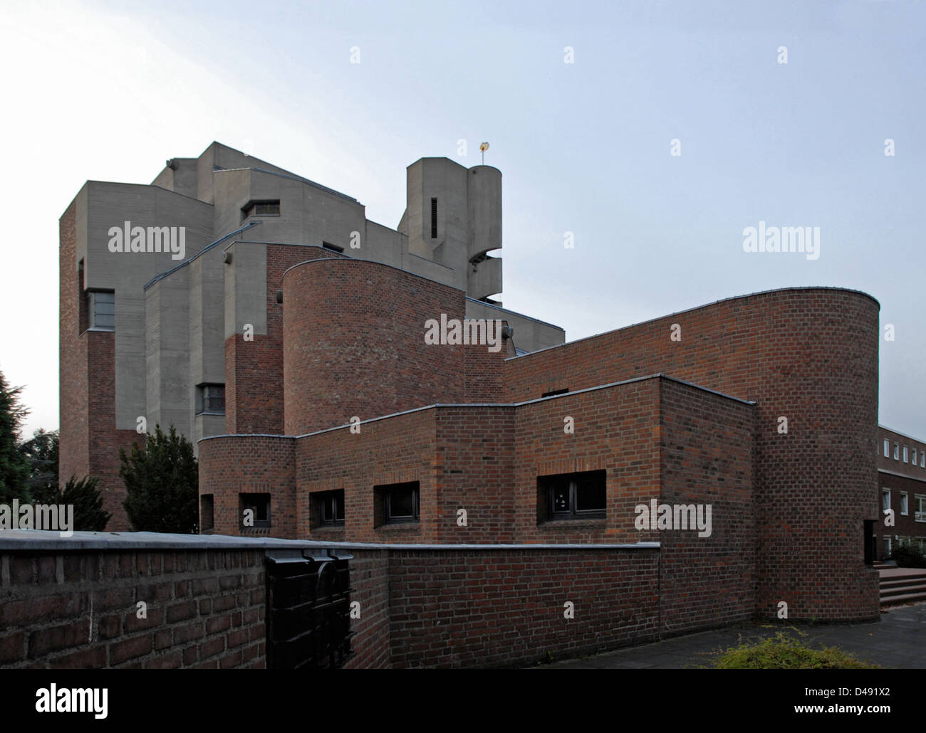 Die Auferstehungskirche, entworfen von Gottfried Böhm in Köln, zwischen 1963 und 1970, ist ein markantes Beispiel brutalistischer Architektur. Die unverwechselbare Fassade aus Beton und Backstein spiegelt Böhms Auseinandersetzung mit Ausdrucksformen wider, indem sie religiöse Symbolik mit moderner Architektursprache verbindet. Stockfoto