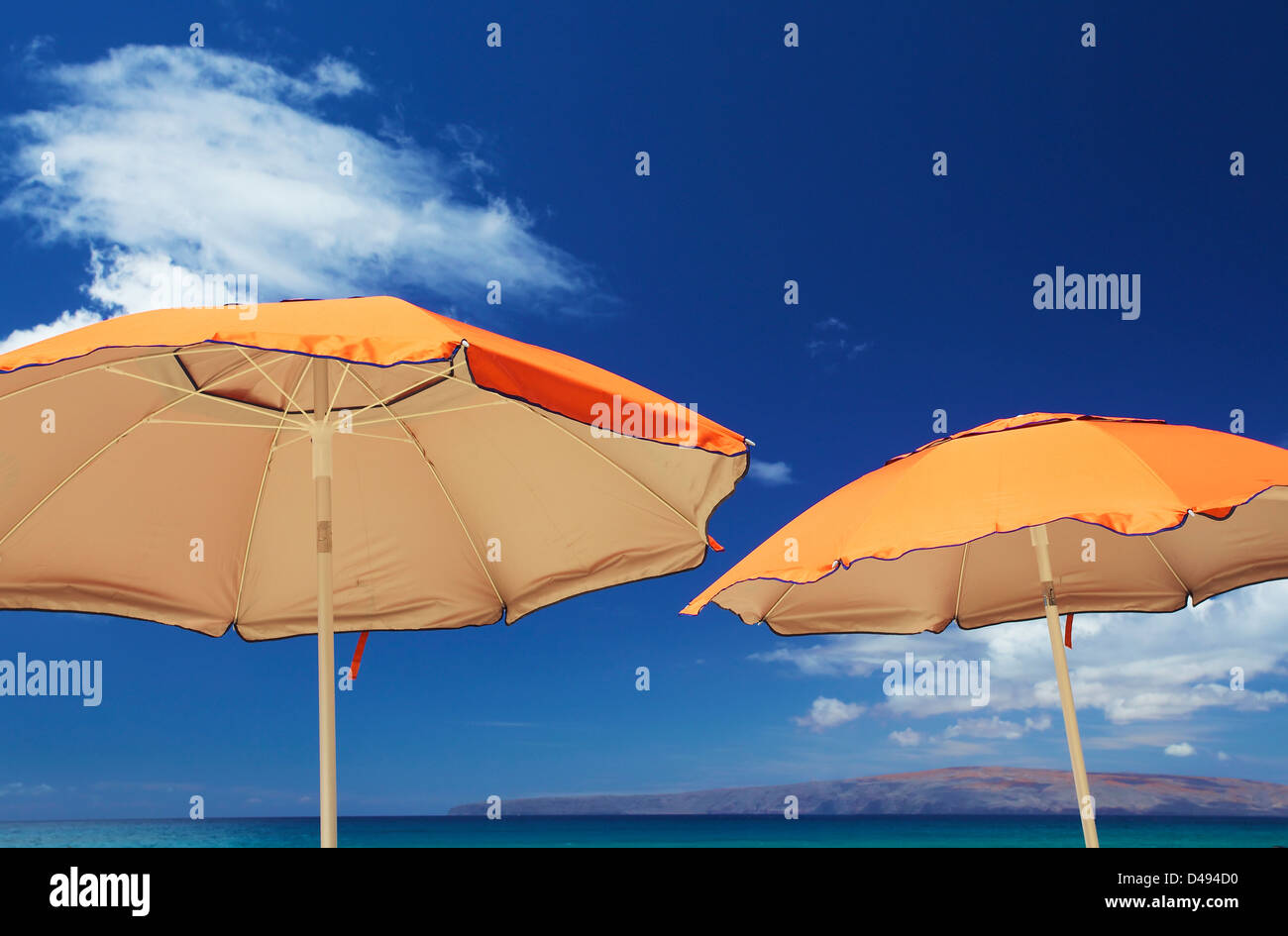 Gelbe Sonnenschirme vor blauem Himmel mit Wolken und Berge an der Küste von einer hawaiischen Insel; Hawaii-USA Stockfoto