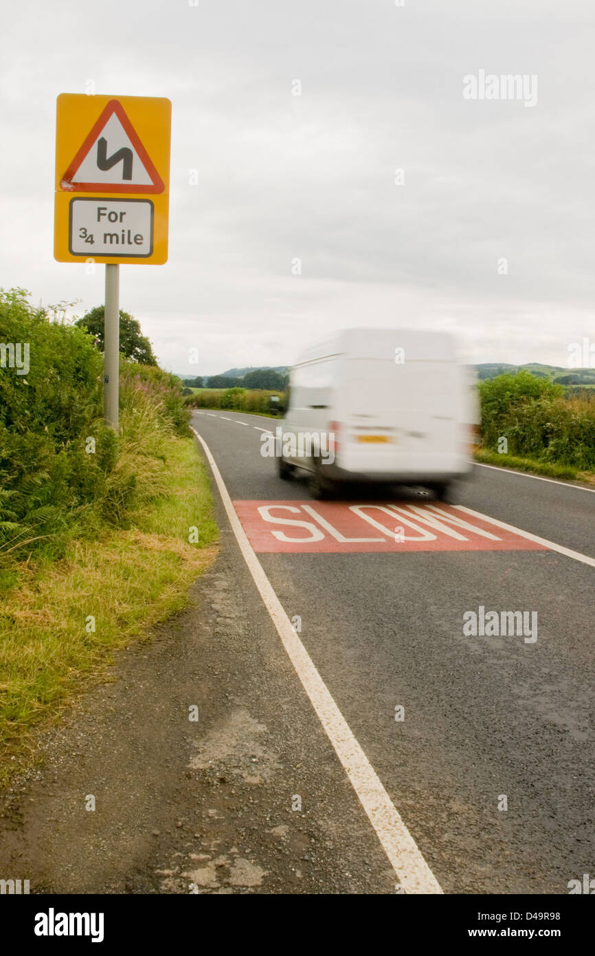 Ein weißer Lieferwagen vorbei an einem langsamen Schild auf einer ländlichen Landstraße in der englischen Landschaft zu beschleunigen. Stockfoto