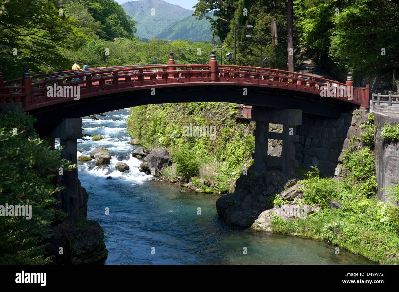 Besucher über die Futarasan Schrein Shinkyo Heilige Brücke über einem klaren Wasserstrom in Nikko, Tochigi, Japan. Stockfoto