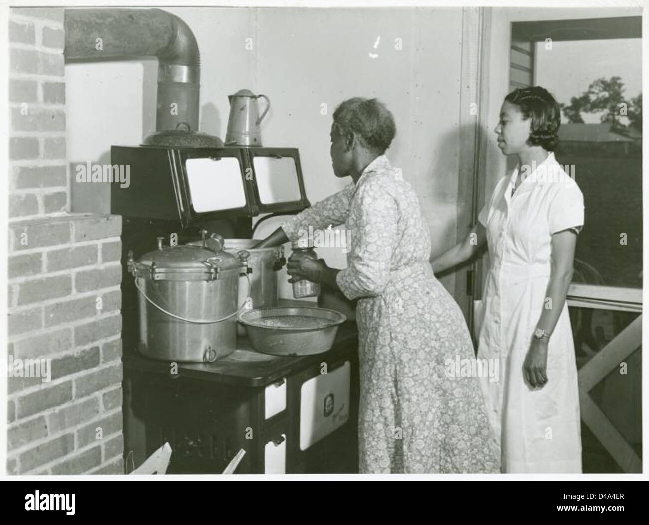Ein Foto aus dem Jahr 1939, das die afroamerikanischen Frauen Ada Turner und Evelyn M. Driver in einer Küche zeigt, die Erbsen als Teil des Hausmanagements und der Öko-Praxis konservieren. Dieses Bild spiegelt das Leben im Haushalt und Techniken zur Konservierung von Lebensmitteln wider. Stockfoto