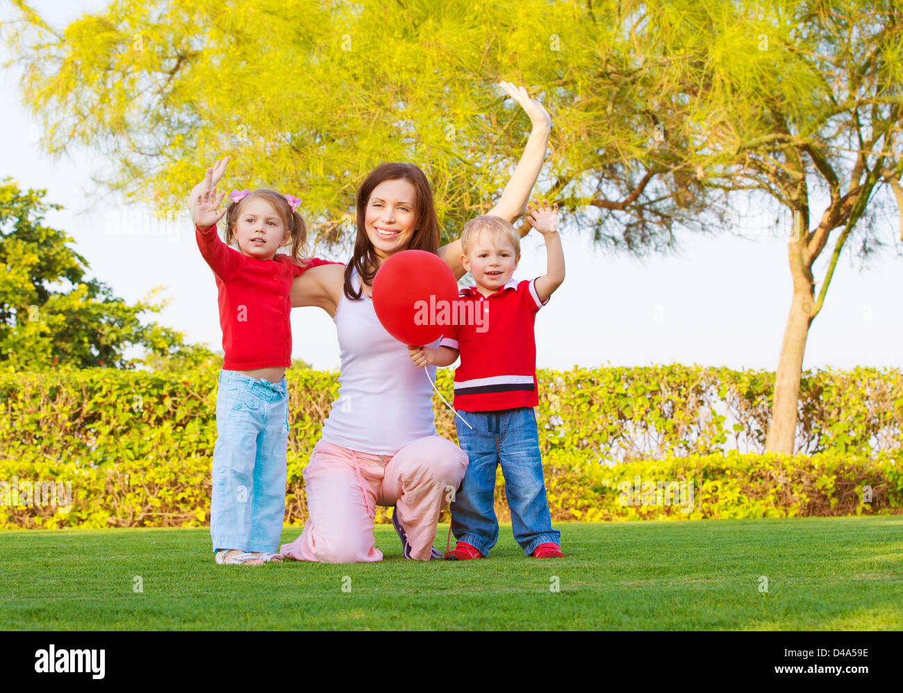 Foto von hübschen Mutter mit zwei niedlichen Kinder erhobenen Hände hoch und genießen Sonnentag, glückliche junge Familie Hand in Frühlingspark winken, Stockfoto