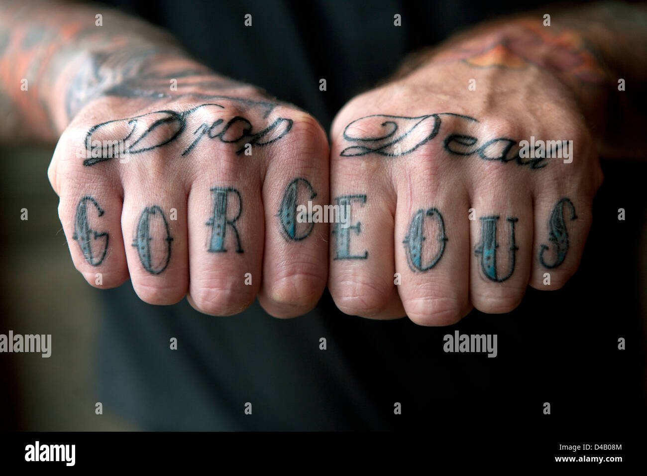 Ein Mann zeigt seine tätowierten Finger & Knöchel mit den Worten "Drop Dead Gorgeous". Stockfoto