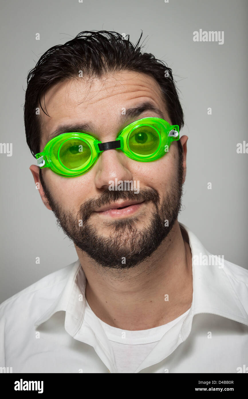 Porträt eines jungen bärtigen Mannes mit grünen Gläsern auf grauem Hintergrund schwimmen Stockfoto