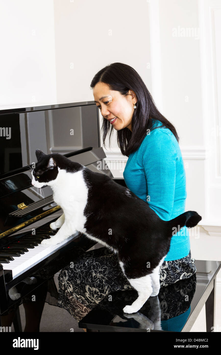 Vertikale Foto Reife Frau, die gerade ihre Familienkatze mit seinen Pfoten auf der Tastatur des Klaviers Stockfoto