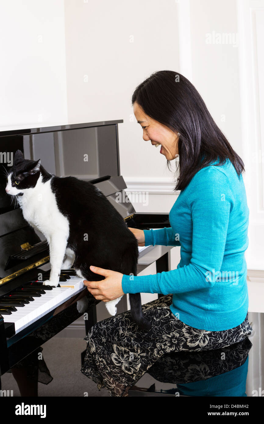 Vertikale Foto Reife Frau lachen bei Familie Katze sitzt am Klavier-Tastatur Stockfoto