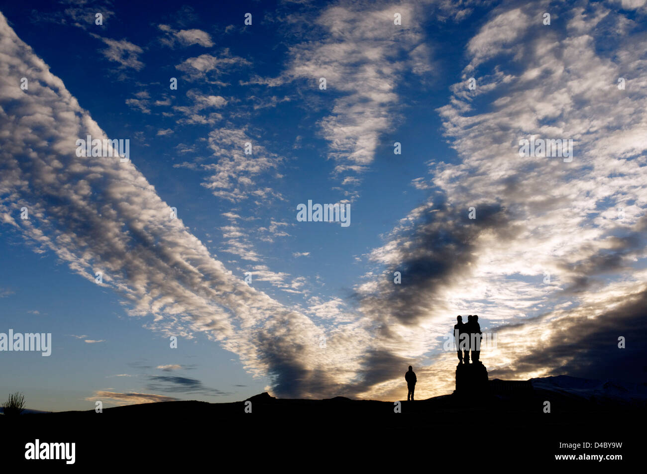 Eine Person, die gegen eine dramatische Sonnenaufgang Wolkengebilde und die Commando-Denkmal am Spean Bridge in den schottischen Highlands Stockfoto