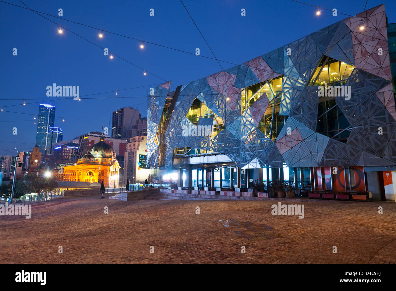 Federation Square bei Nacht mit Flinders Street Station im Hintergrund beleuchtet. Melbourne, Victoria, Australien Stockfoto