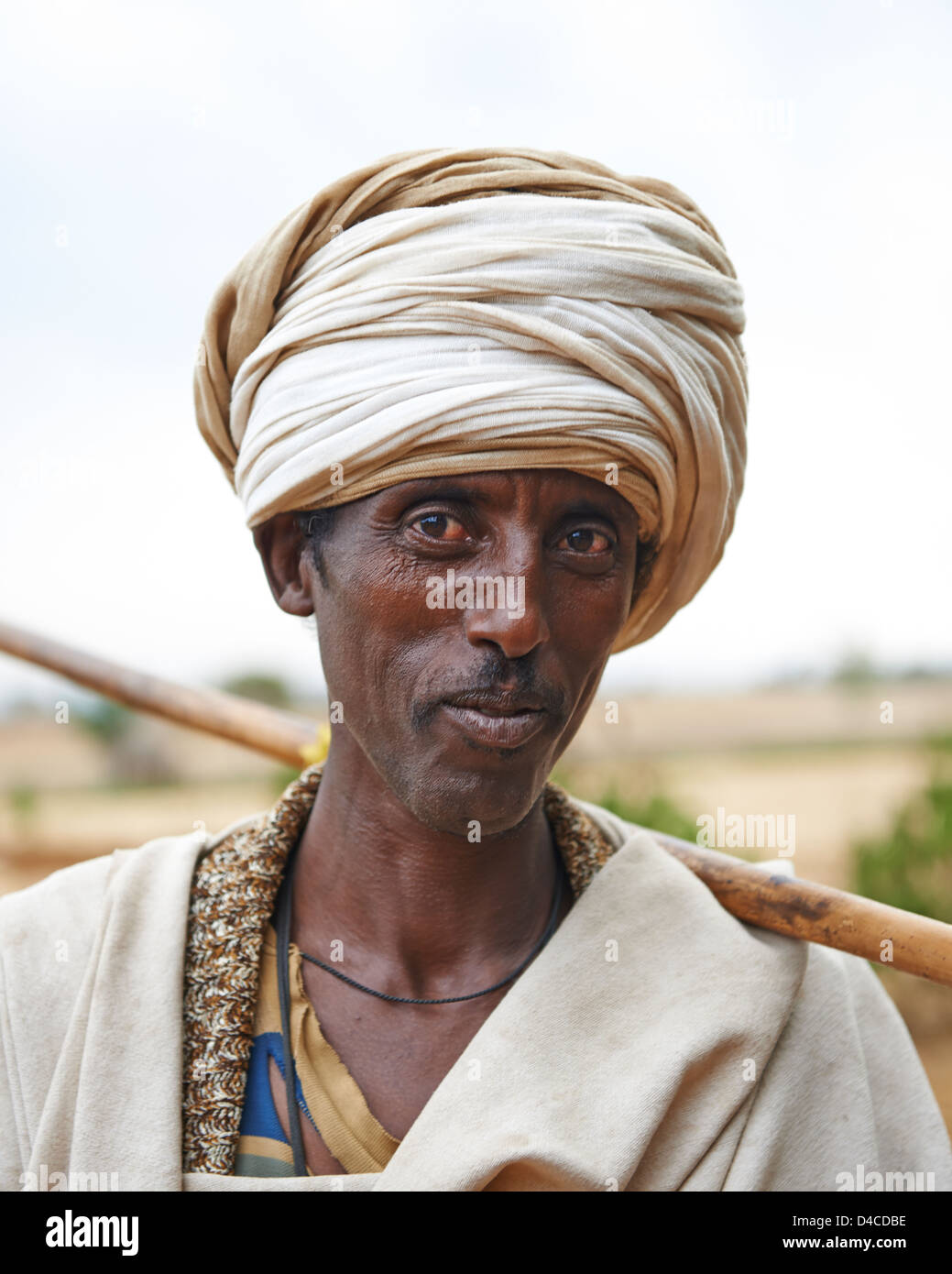 Ein Mann mit einem Gehstock und Turban geht auf einem Feldweg Stockfoto