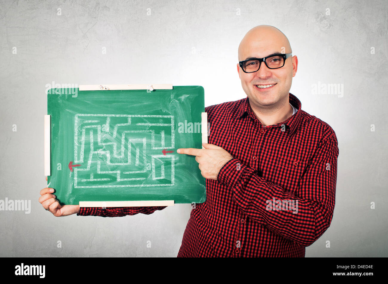 Junge Erwachsene Glatzkopf mit Brille hält eine kleine grüne Tafel mit Labyrinth, den richtigen Weg zu zeigen. Stockfoto