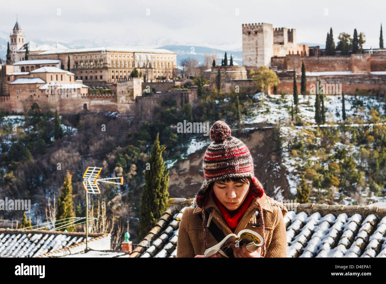 Weibliche japanische Touristen einen Reiseführer mit schneebedeckten Alhambra-Palast im Hintergrund zu lesen. Granada, Spanien Stockfoto