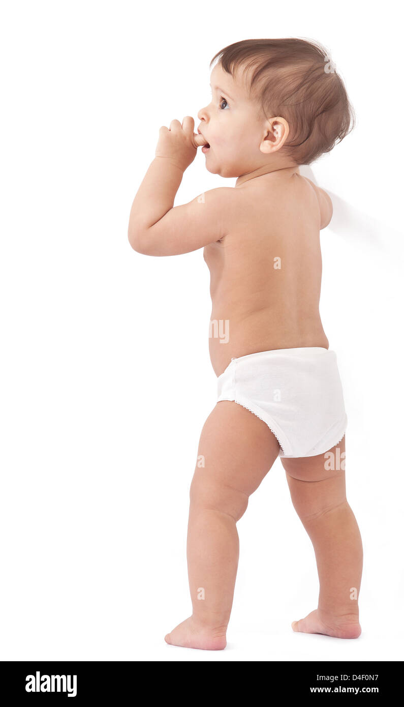 Lustige Baby bleibt in der Nähe von Wand und Finger in den Mund hält. Isoliert auf weißem Hintergrund. Stockfoto