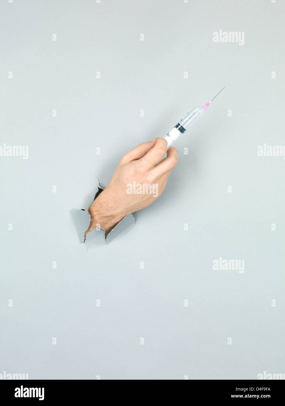 Nahaufnahme der männlichen Hand mit einer Spritze durch ein zerrissenes Papier grau Stockfoto
