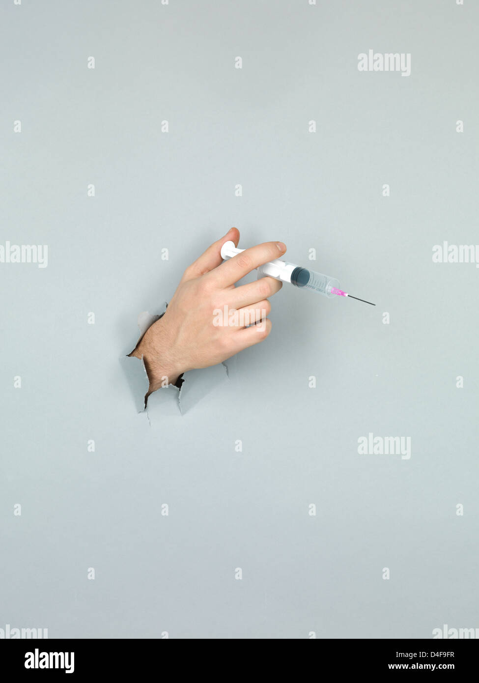Nahaufnahme der männlichen Hand Holding eine Spritze durch ein zerrissenes Papier grau Stockfoto
