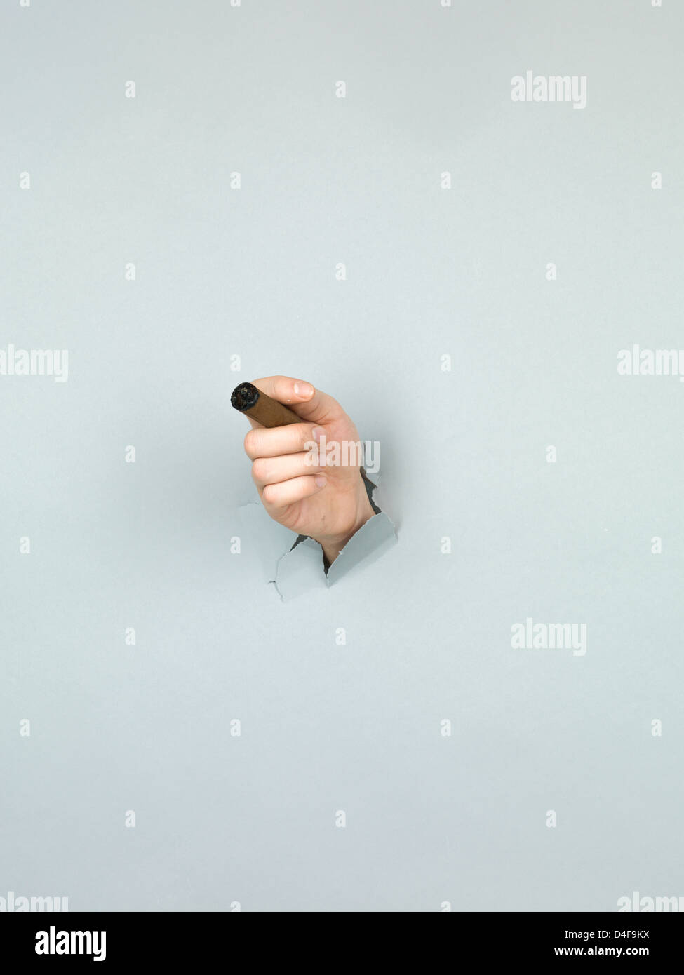 Nahaufnahme der männliche Hand, die eine Zigarre durch ein zerrissenes Papier grau Stockfoto