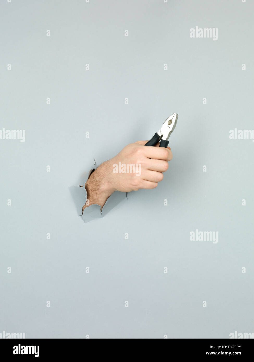 Nahaufnahme der männlichen Hand mit einer Zange durch ein zerrissenes Papier grau Stockfoto