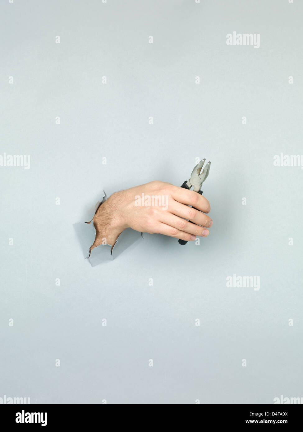 Nahaufnahme der männlichen Hand mit einer Zange durch ein zerrissenes Papier grau Stockfoto