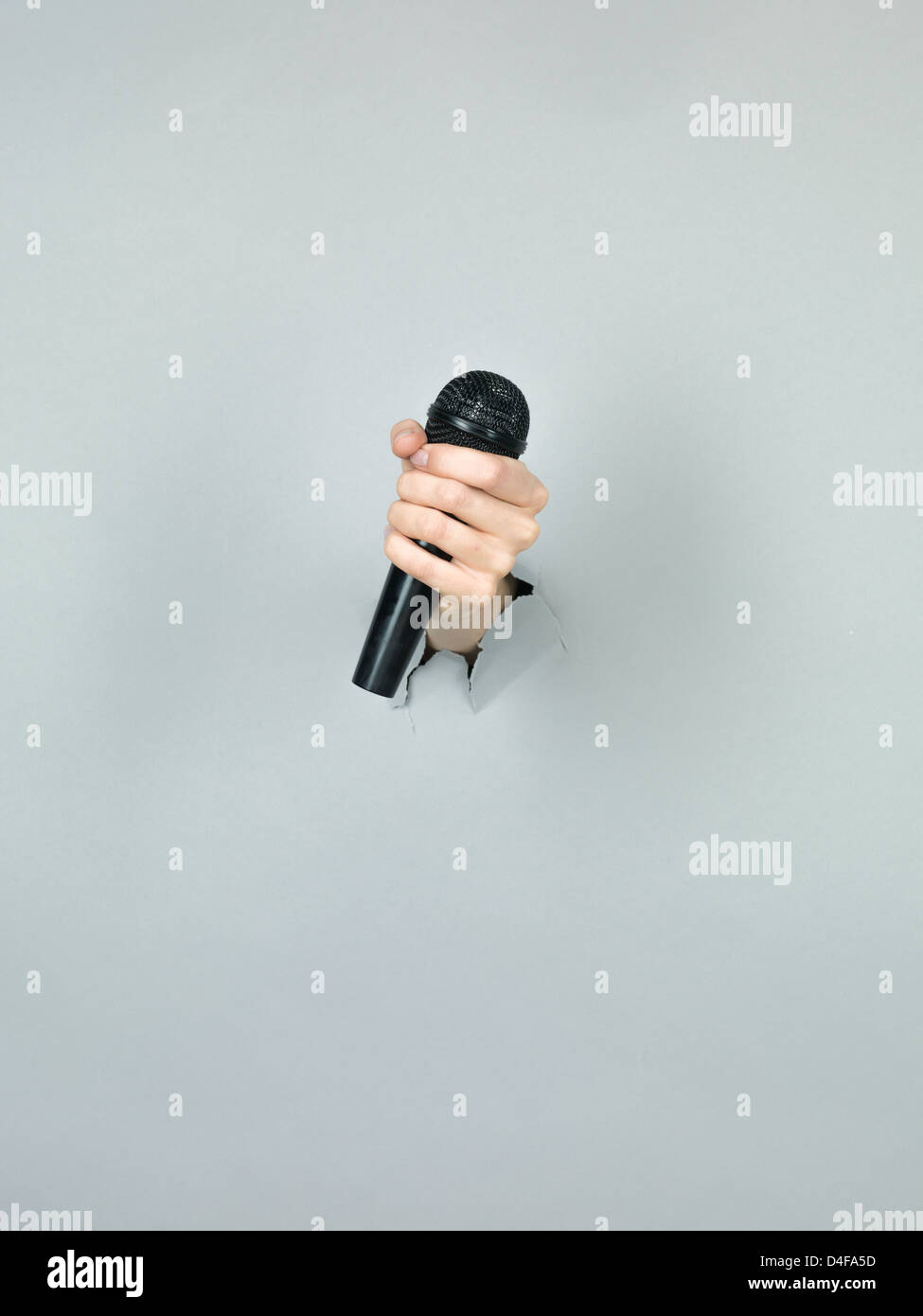 Nahaufnahme eines Mädchens Hand hält ein schwarzes Mikrofon durch ein zerrissenes Papier grau Stockfoto