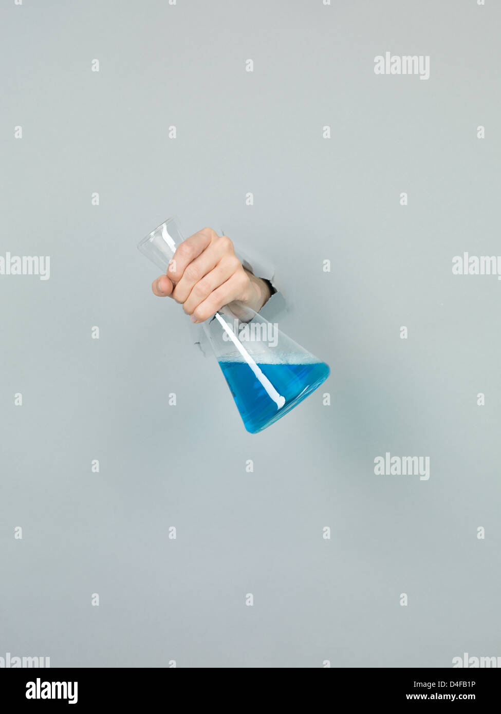 Nahaufnahme des weiblichen Hand hält eine Chemie-Flasche mit blauen Flüssigkeit darin durch ein zerrissenes Papier grau Stockfoto