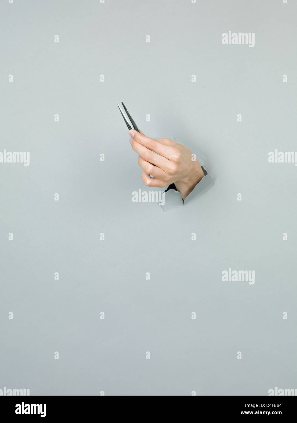 Nahaufnahme von weiblicher Hand mit einer Pinzette durch ein zerrissenes Papier grau Stockfoto