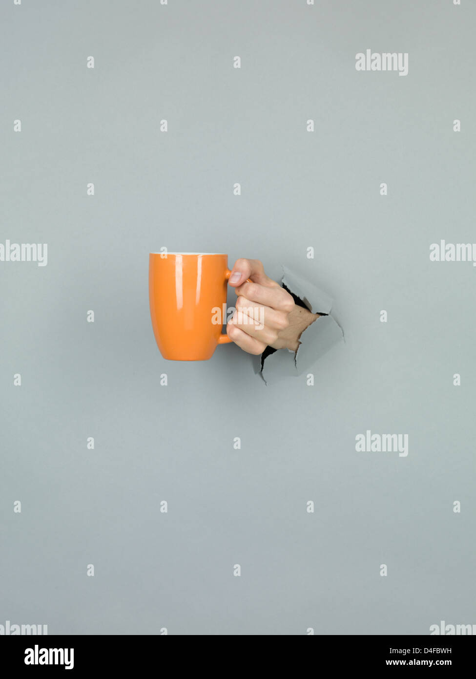 Nahaufnahme des weiblichen Hand holding eine orange Schale durch ein zerrissenes Papier grau Stockfoto