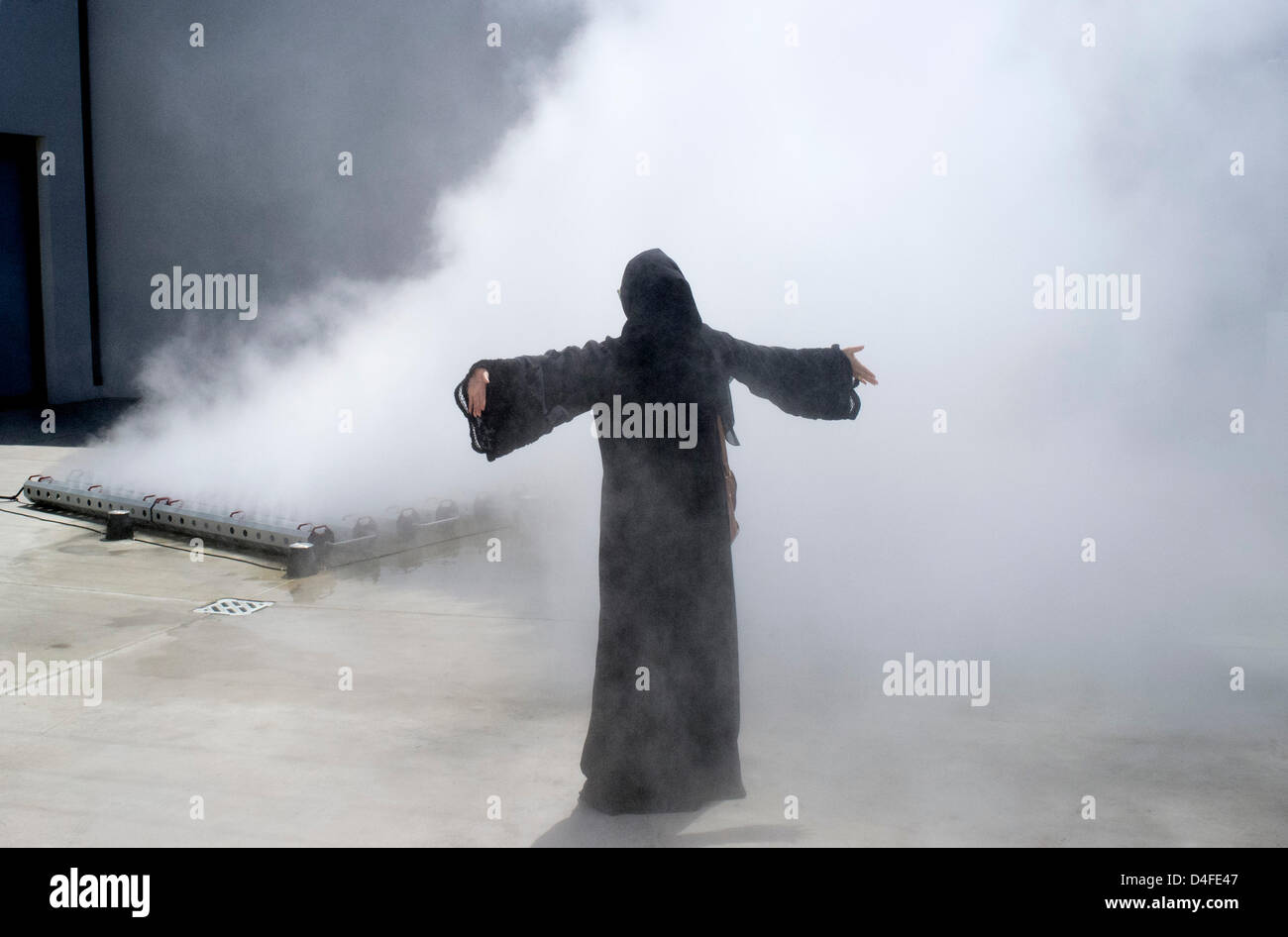 Besucherin in Black Abaya, die sich am Eröffnungstag des 11. in den Vereinigten Arabischen Emiraten stattfindenden Kunst- und Kulturfestivals Sharjah Biennial 2013 unter Wassernebel abkühlt Stockfoto