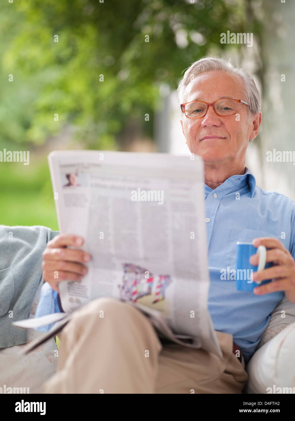 Mann liest Zeitung im Veranda-Schaukel Stockfoto