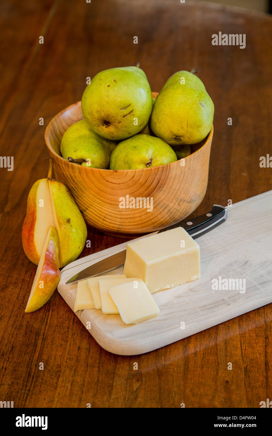 Eine Schale mit frischen Bartlett Birnen auf einem Holztisch mit Schnittkäse und ein Schälmesser auf ein Holz Schneidebrett und eine geschnittene Birne Stockfoto