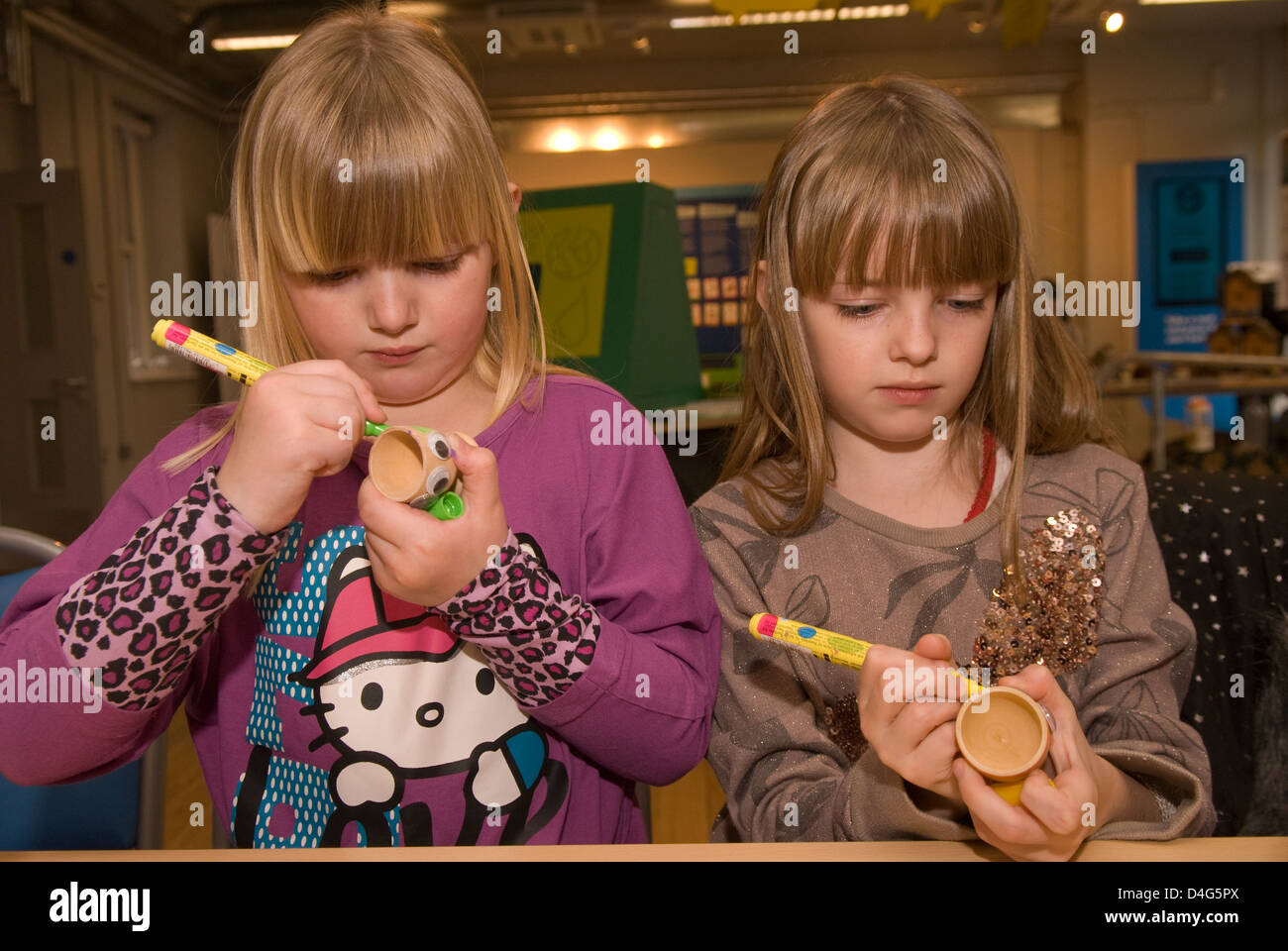 Zwei Schwestern, 6 & 7 Jahre alt, dekorieren Eierbecher an einem eco station Tag der offenen Tür, Bordon, Hampshire, UK. Stockfoto