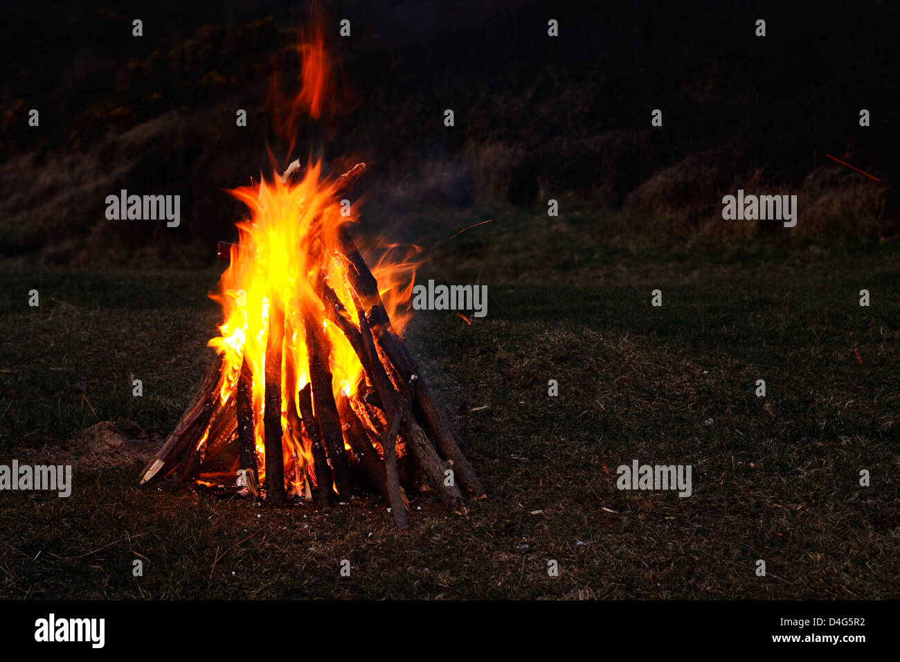 Knisternden Lagerfeuer von echtem Holz gesammelt, am Strand und in voller Glut mit dunklem Hintergrund für Kopie Stockfoto