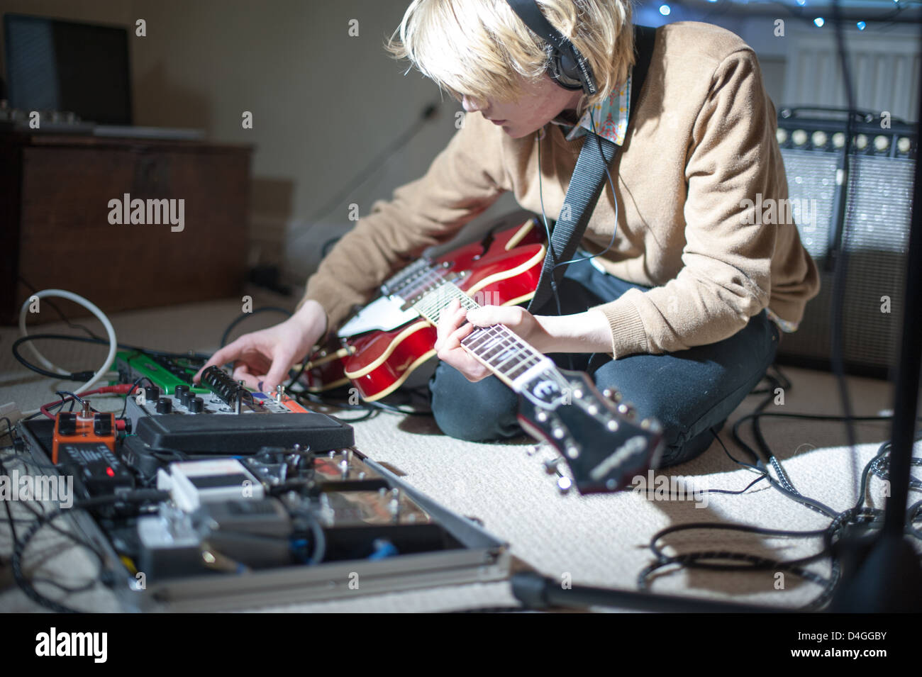 Jungen blonden Musiker mit einem kirschroten Epiphone und eine Pedalklaviatur trägt Kopfhörer und drückt Tasten selbst aufzeichnen Stockfoto