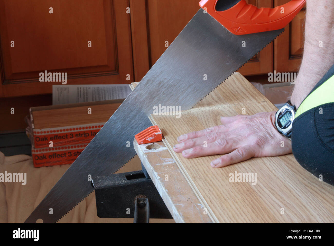 Ein Mann sägt einen Streifen Laminat, der für die Installation eines neuen Bodens bereit ist. Er benutzt eine Handsäge und einen Arbeitskollegen. Stockfoto