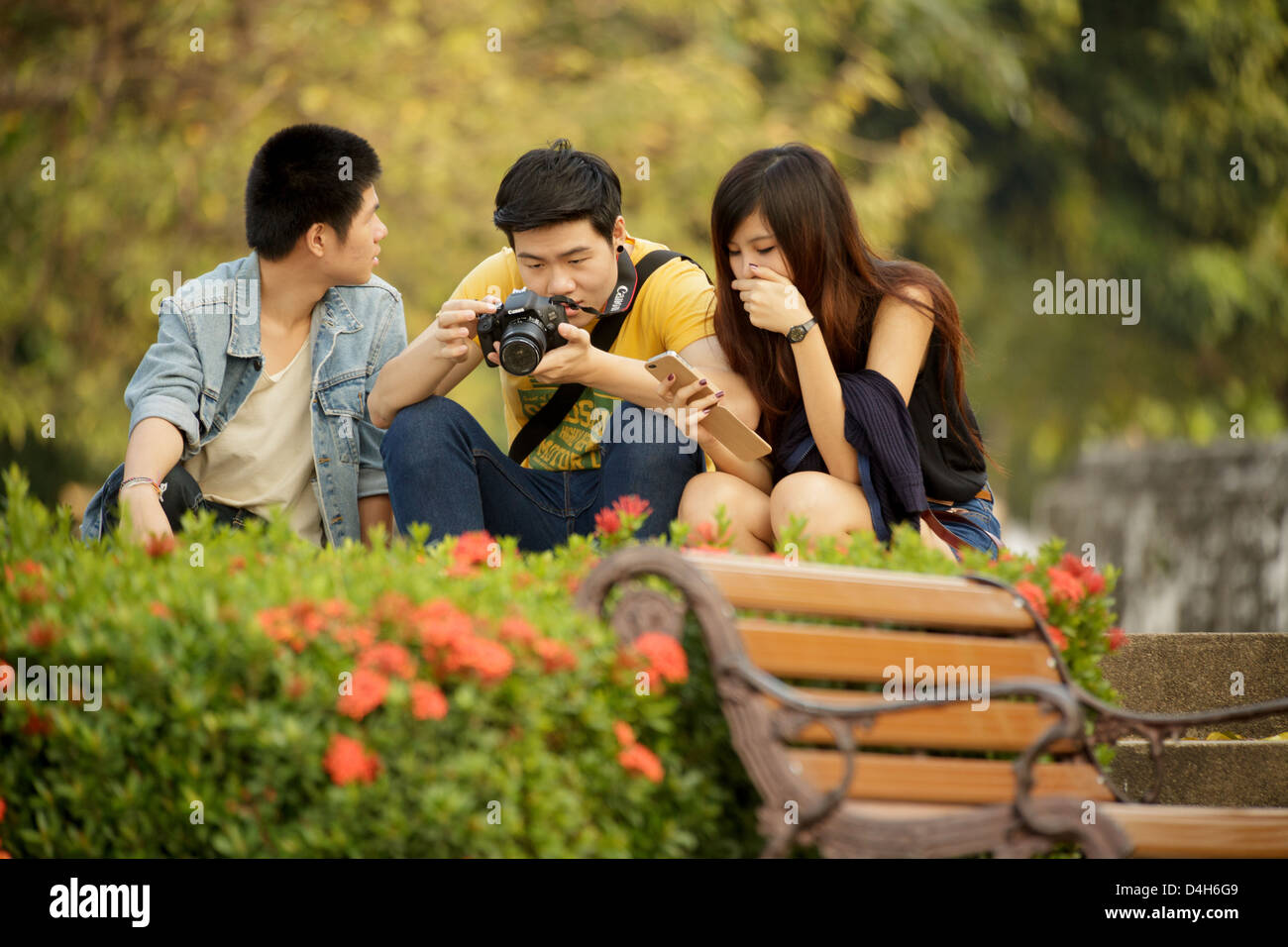 Drei Leute sitzen im Park, sieht man die Fotos vor der Kamera, Bangkok, Thailand Stockfoto