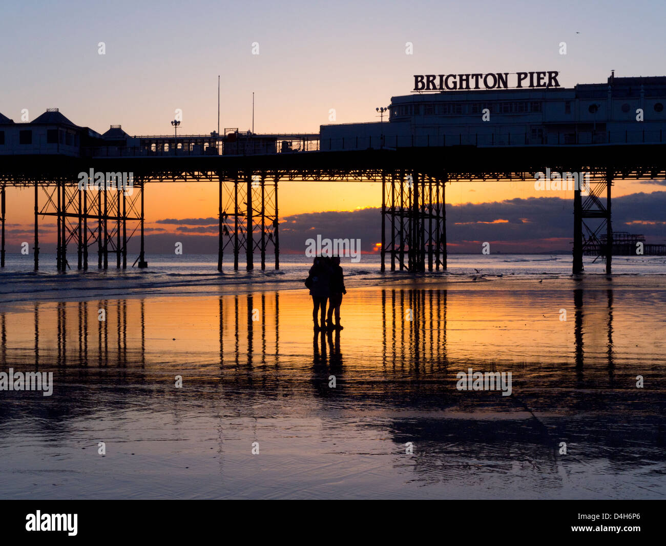 Brighton Pier bei Sonnenuntergang, goldenen Himmel reflektiert den Sand bei Ebbe Stockfoto