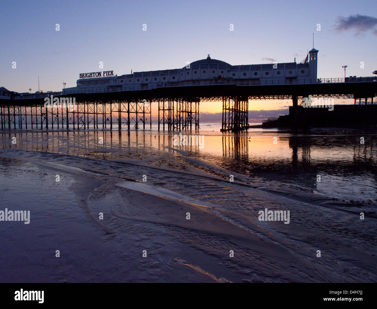 Brighton Pier bei Sonnenuntergang, goldenen Himmel reflektiert den Sand bei Ebbe Stockfoto