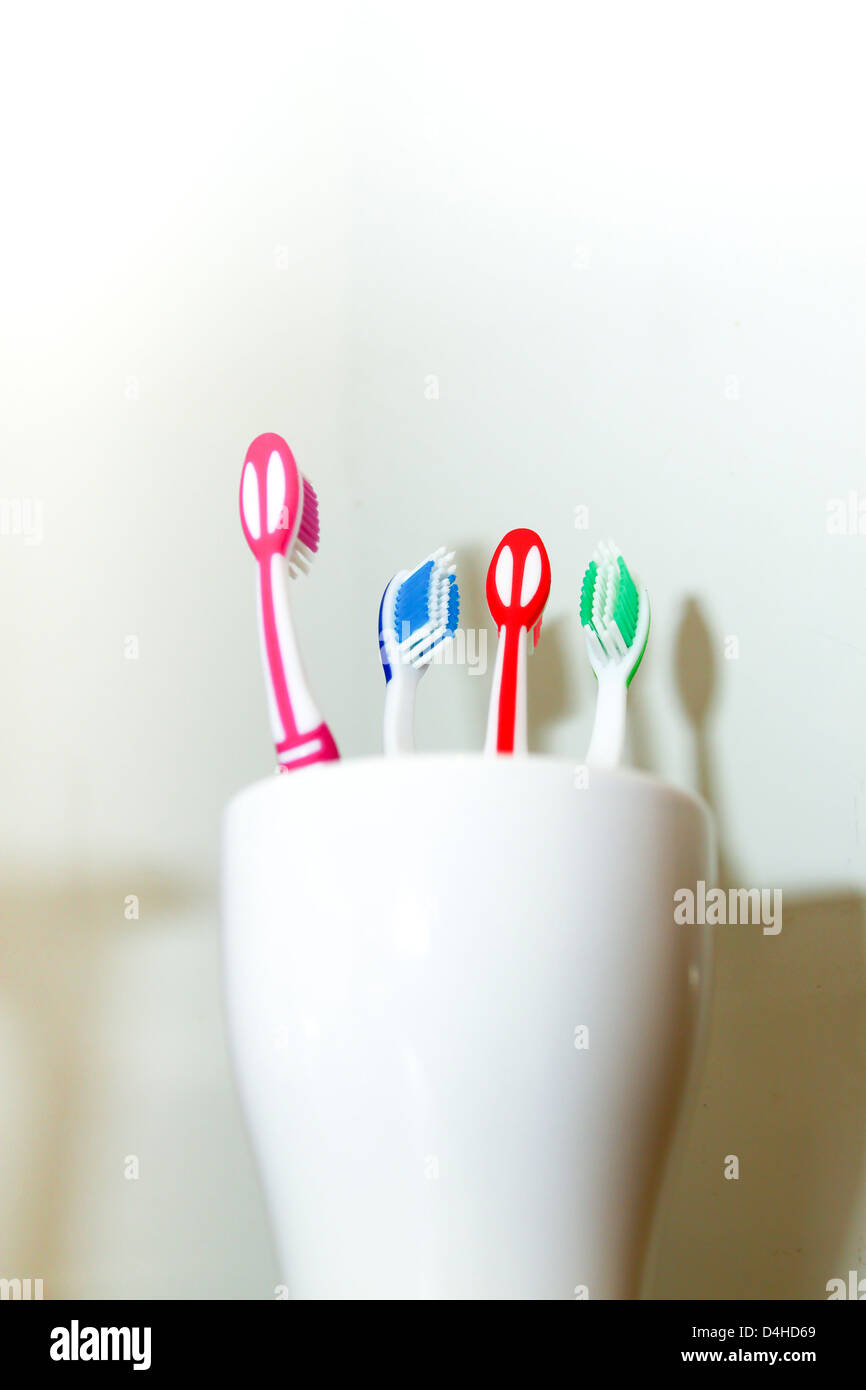 Vier verschiedene farbige Zahnbürsten in weiße Tasse Stockfoto