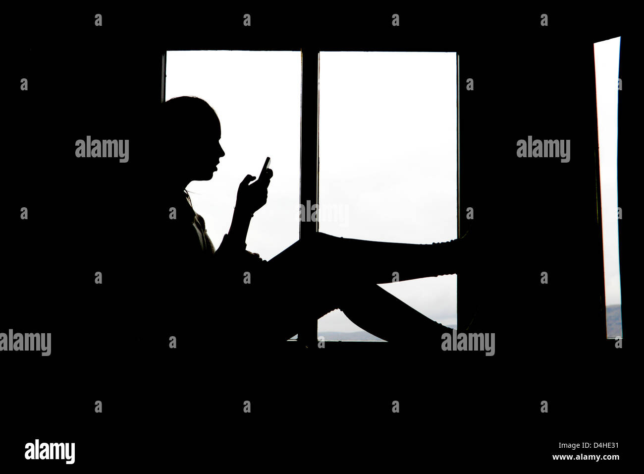 Junge Teenager-Mädchen sitzen im Fenster SMS auf Handy Stockfoto