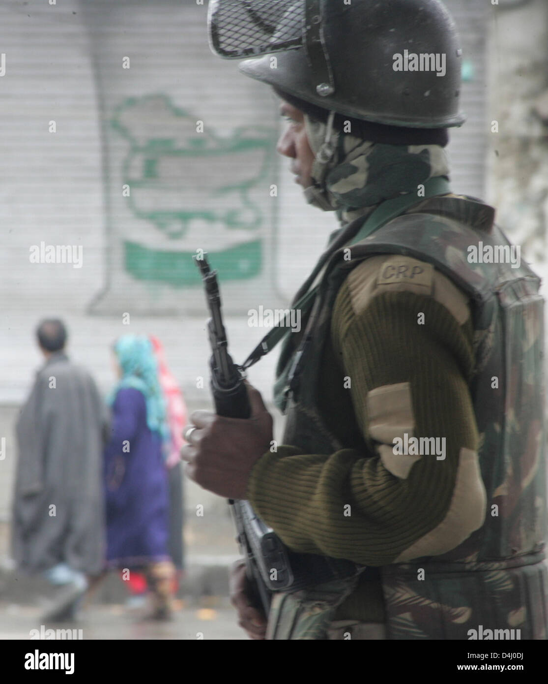 Srinagar, indisch verwalteten Kaschmir, Donnerstag, 14. März 2013. Eine Gruppe von kaschmirische Muslime gehen vorbei an einen Shop mit Karte von Kaschmir gemalt, wie eine indische paramilitärischer Soldat steht Wache während eine Ausgangssperre in Srinagar im Sommer, die Hauptstadt des indischen Kaschmir, Indien verabreicht. Indische Behörden verhängte Ausgangssperre in Kaschmir, die Protestdemonstration zu vereiteln, nachdem sie einen 34 Jahre alten Mann am Mittwoch getötet. Foto von Sofi Suhail/Alamy) Stockfoto