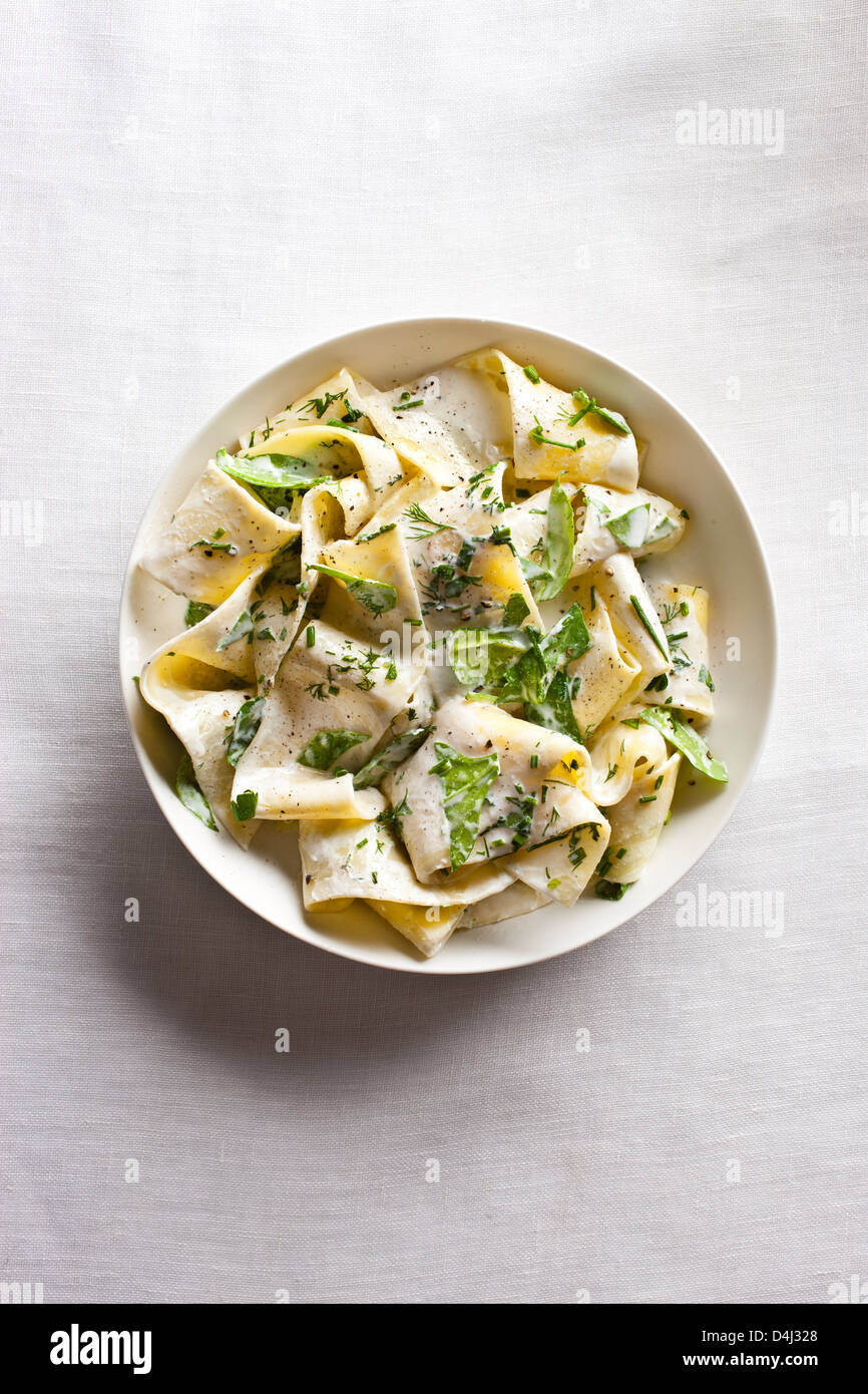 Ein Teller mit Pappardelle Pasta mit cremigem Ricotta, Baby-Spinat, frischen Kräutern und Pfeffer. Stockfoto