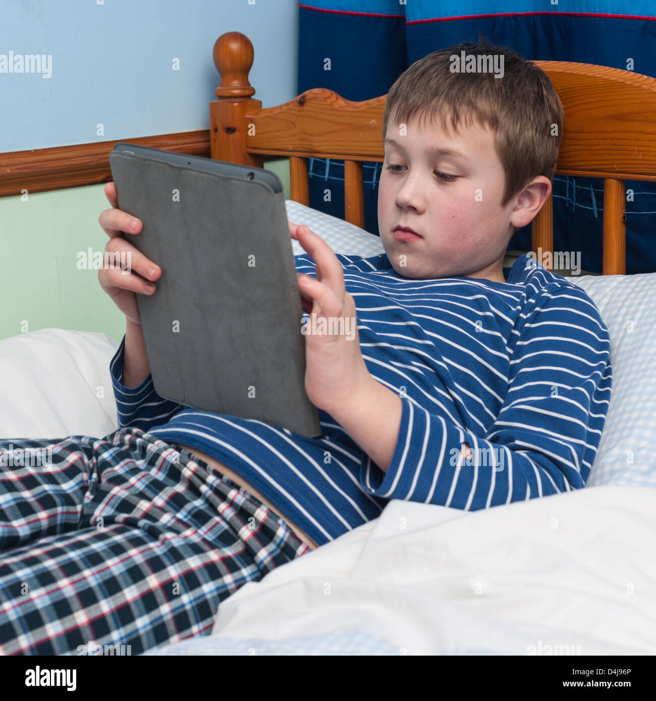 Ein neun Jahre alter Junge mit seinem Ipad Tablet in seinem Schlafzimmer Stockfoto