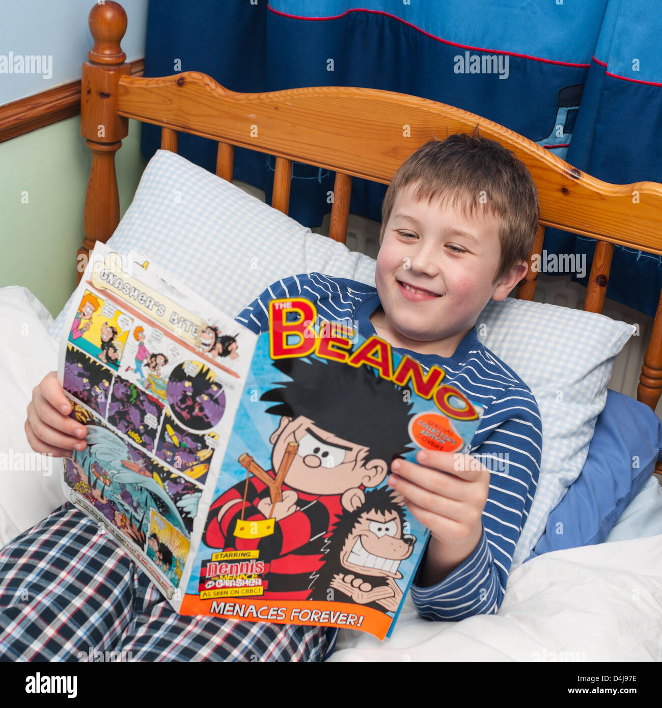 Ein neun Jahre alter Junge liest Beano Comic in seinem Schlafzimmer Stockfoto