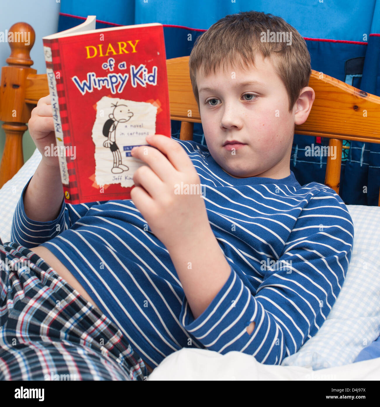 Ein neun Jahre alter Junge liest Diary of a wimpy Kid-Kinder-Buch in seinem Schlafzimmer Stockfoto