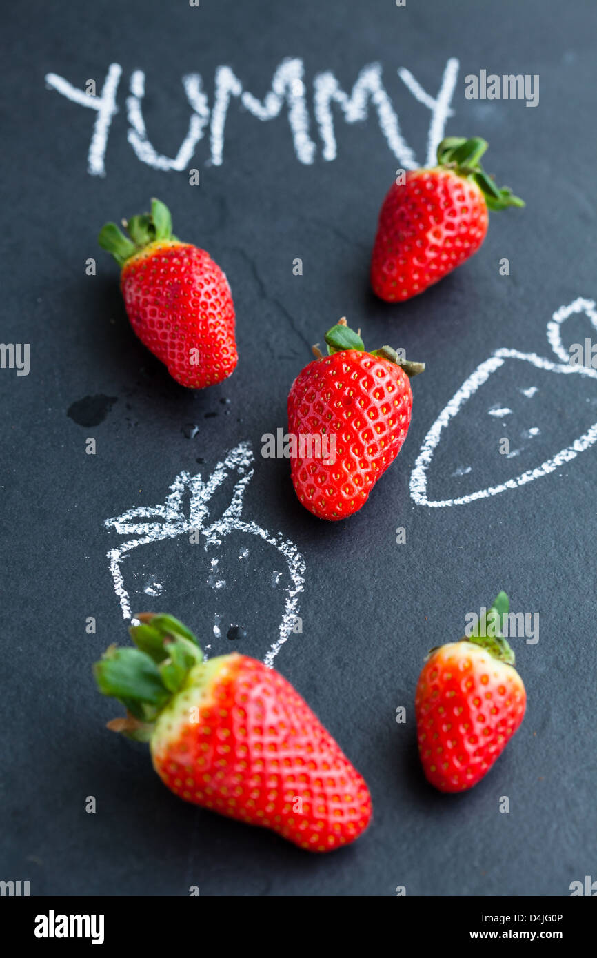 Ganze Erdbeeren und Kreidezeichnungen und lecker Wort auf dunklem Hintergrund Stockfoto