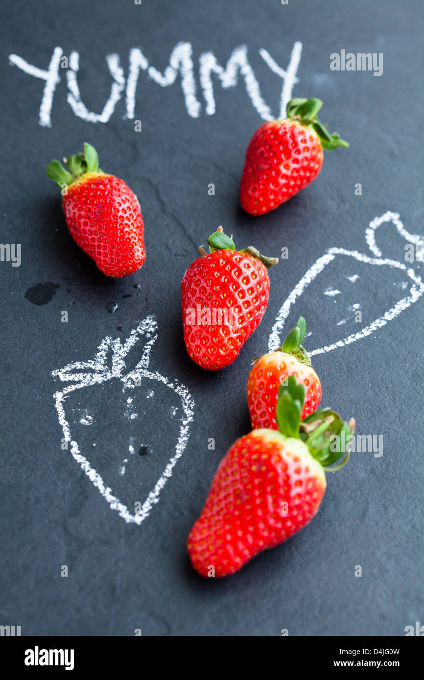 Ganze Erdbeeren und Kreidezeichnungen und lecker Wort auf dunklem Hintergrund Stockfoto